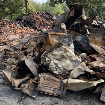 Kahden kuvan yhdistelmä, jossa vasemmalla on kuva sinisestä puutalosta ja oikealla tulipalon jäljiltä metalliromua ja tiiliä.