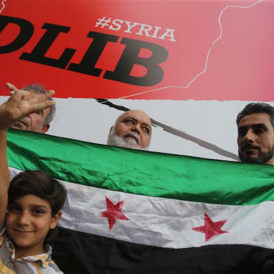 Ihmisiä Vapaan Syyrian lipun edessä, takana Idlib-kyltti