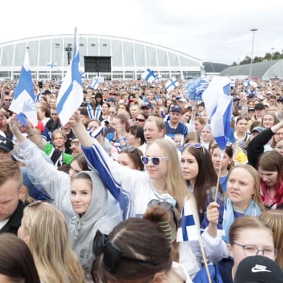 Hakametsän hallin edustalla parkkialue täynnä ihmisiä, joista iso osa heiluttaa Suomen lippuja.