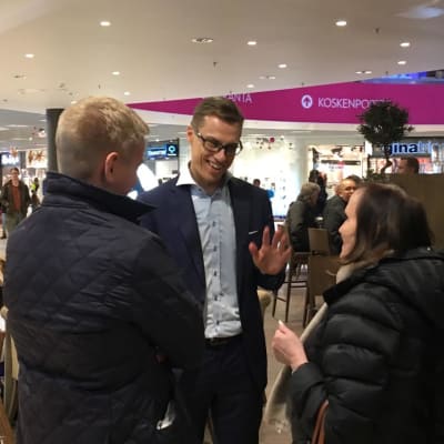 Alexander Stubb puhuu ihmisten kanssa märässä paidassa
