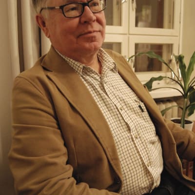 Pekka Poutanen sitter i en stol vid ett fönster.