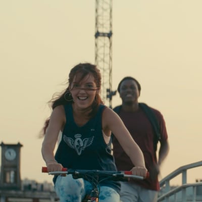 En flicka cyklar och en pojke springer bakom henne med blicken riktad mot kameran.