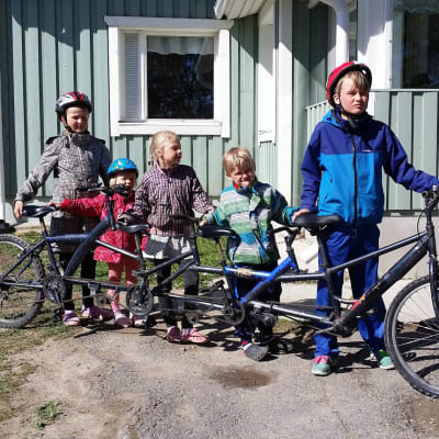 Kuvassa neljä lasta ja pyörä, jossa on neljä paikkaa.