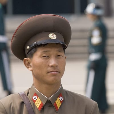 Pohjoiskorealainen sotilas katsoo kameraan. Takana epäselvänä hahmona Etelä-Korea sotilas. 