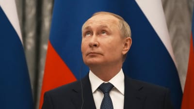 En man i kostym, Rysslands president Vladimir Putin, tittar uppåt framför en rysk flagga.