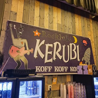Suuri siniharmaa kyltti, jossa lukee "Rocklubi Kerubi". Kyltissä myös piirros kitaraa soittavasta henkilöstä, raketista ja planeetoista. Kyltin alapuolella kylmäkaappeja, joissa juomia sekä juomalaseja.