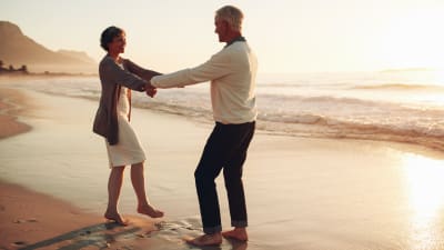 Äldre kvinna och man dansar på sandstrand