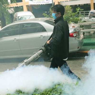 Terveysviranomainen kantaa hyttysten torjuntamyrkkyä suihkuttavaa ruiskua Bangkokin kadulla. Kemikaalia näkyy ilmassa.