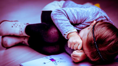 En liten flicka ligger och gråter.