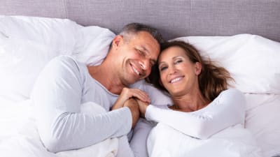 Leende man och kvinna ligger i en säng