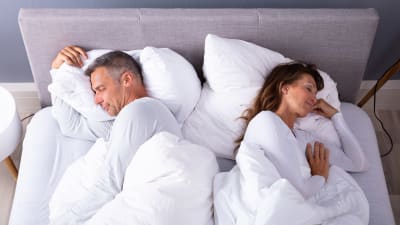 man och kvinna sover med ryggarna mot varandra, både belåtet leende