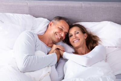 Leende man och kvinna ligger i en säng