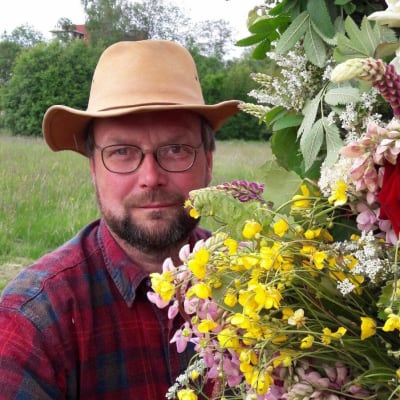 en man i hatt och rutig skjorta håller i en stor blombukett av vilda blommor i en blomsteräng