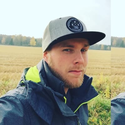 En man iklädd keps och blå jacka står ut på ett fält. Det ser ut att vara höst.