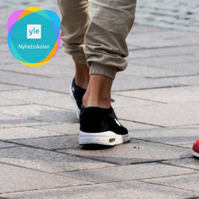 Två personer promenerar med korta byxor som lämnar vristerna bara. Yle Nyhetsskolans logo i vänstra övre hörnet.