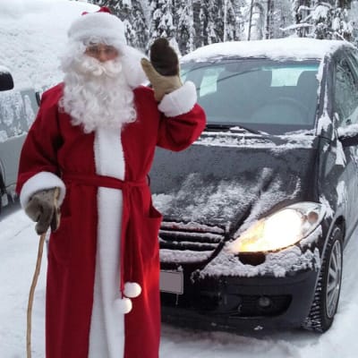 Riku Oikarinen, 21, on pukeutunut joulupukiksi ja vilkuttaa kameralle. Hänen takanaan on auto ja luminen maisema.
