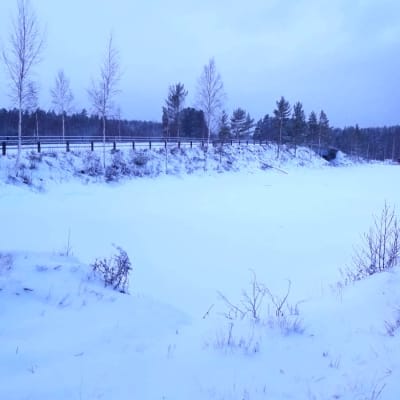 Luminen rantamaisema, jossa jäässä oleva järven poukama ja vieressä kulkee pengertie.