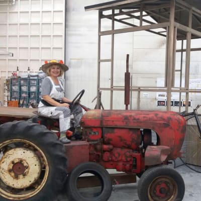 Lotta Kare sitter på en gammal traktor med en blommig hatt på huvudet