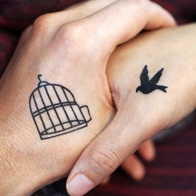Kuvassa kaksi kättä kosettavat toisiaan. Toiseen käteen on tatuoitu häkki, toiseen käteen lintu. 