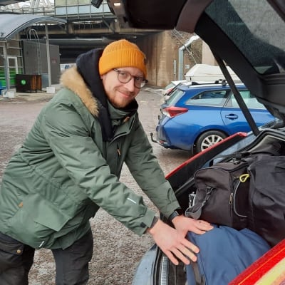 Bilisten Eero Jaakkola ikläd en dunjacka och yllemössa skuffar in sportväskor i bilens baklucka.