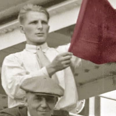 Suomalaissiirtolainen heiluttaa punalippua ja laulaa työläismarssia laivan lähtiessä kohti Amerikkaa (1930-l).