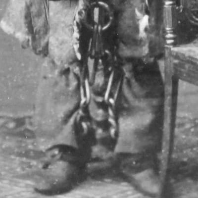 Ett gammalt svartvitt fotografi. Man ser benen och fötterna på en man. Han är fastkejdad med tunga kedjor.