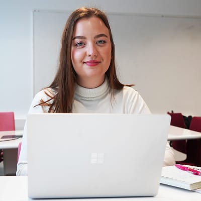 Studerande som sitter framför en bärbar dator i ett tomt klassrum.
