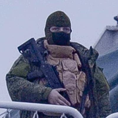 En soldat i full utrustning håller i ett gevär. Han har en mask över ansiktet.