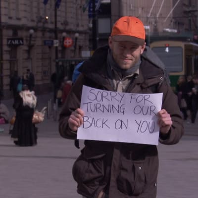 En man med lappen "Sorry for turning our back on you"