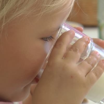 Liten flicka dricker mjölk ur ett glas.