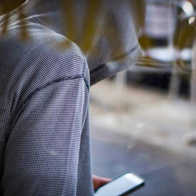 En ung person i munkjacka sitter lutad över en mobiltelefon.