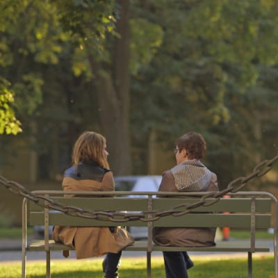 Nuorempi ja vanhempi nainen istuu vierekkäin puistonpenkillä.