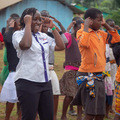 Joukko kenialaisia tanssii iloisesti, etualalla kaksi naista ja lasta.