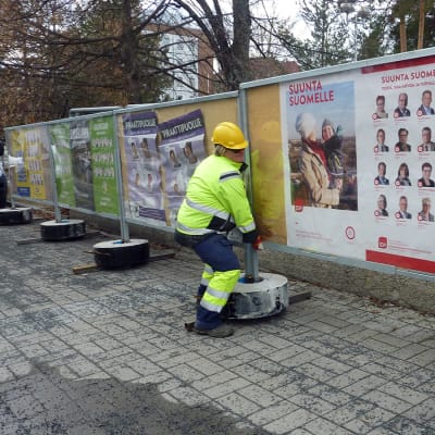 Huoltomiehet nostavat vaalimainonta julistetta pois paikaltaan.