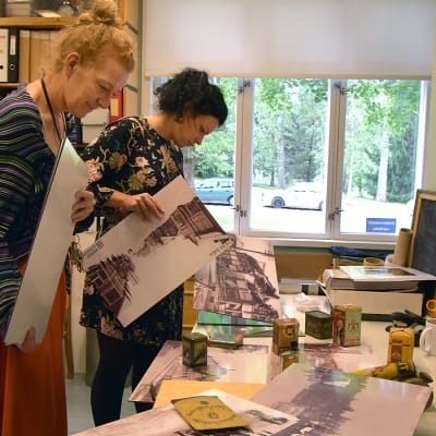 Kaksi naista tutkii valokuvatauluja museon toimistossa