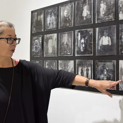 Taiteilija tarkastelee työtään, joka esittelee vanhoja mustavalkoisia valokuvia