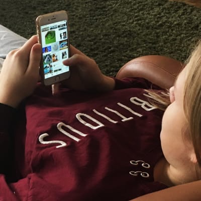 Tyttö löhöää nojatuolissa ja selaa kännykällä Instagramia
