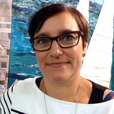 En kvinna med mörkt kort hår och svarta glasögon ler mot kameran.