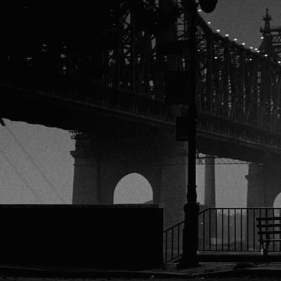 Isaac ja Mary (Woody Allen ja Diane Keaton) istuvat puistonpenkillä selin kameraan katsellen valaistua siltaa. Kuva elokuvasta Manhattan