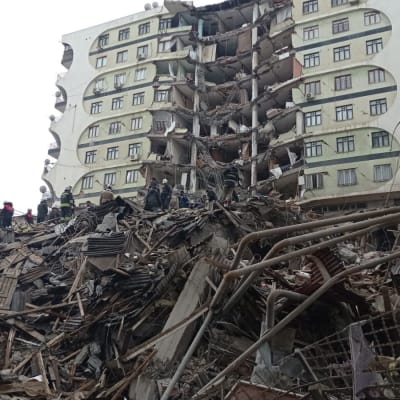 Människor och räddningspersonal söker efter offer på platsen för en kollapsad byggnad efter en kraftig jordbävning i Turkiet.