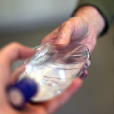 En hand tar emot en genomskinlig flaska av en annan hand.