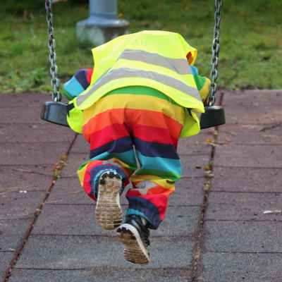 Lapsi keinuu värikkäissä vaatteissa päiväkodin keinussa.