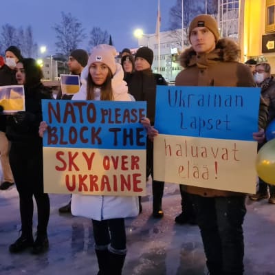 Ihmisiä seisoo torilla kyltit käsissään. Kylteissä toivotaan Naton suojaavan Ukrainaa lentokoneillaan ja kerrotaan, että Ukrainan lapset haluavat elää.