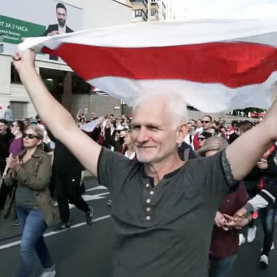 Ales Bialiatski går i tåg med människor omkring sig och håller upp den rödvita flaggan som används i demonstrationerna i Belarus. 