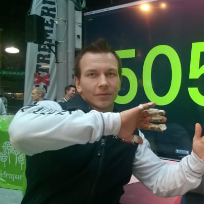 Joonas Mäkipelto poseeraa tulostaulun edessä.