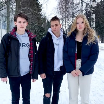 Tre ungdomar står på en snöig trottoar.