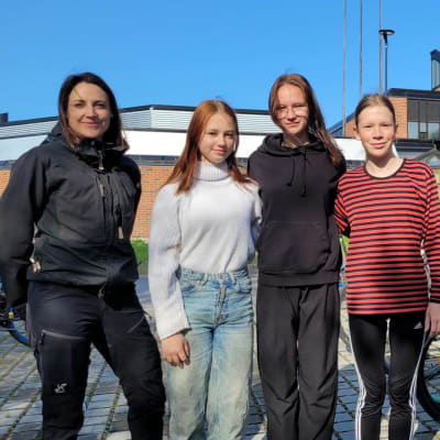Mies ja nainen sekä kolme 7-luokkalaista vaasalaistyttöä seisoo Vaasalaisen Variskan yhtenäiskoulun pihalla ja katsoo kameraan