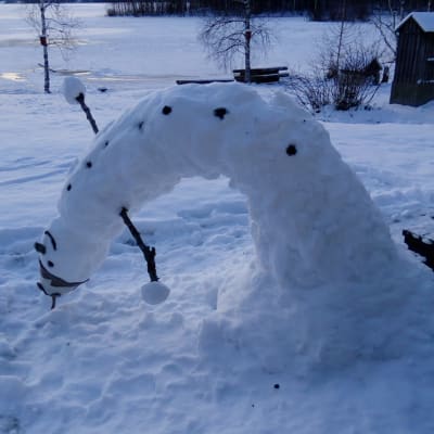 Kuvapari, jossa kapea ja korkea lumiukko on mennyt kaarelle toiselle kyljelleen.