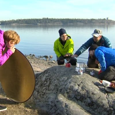 Kolme testaaja ja toimittaja katsovat retkikeittimiä kalliolla
