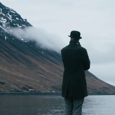 En ryggtavla av en stående man som betraktar en isländsk fjord från stranden.
